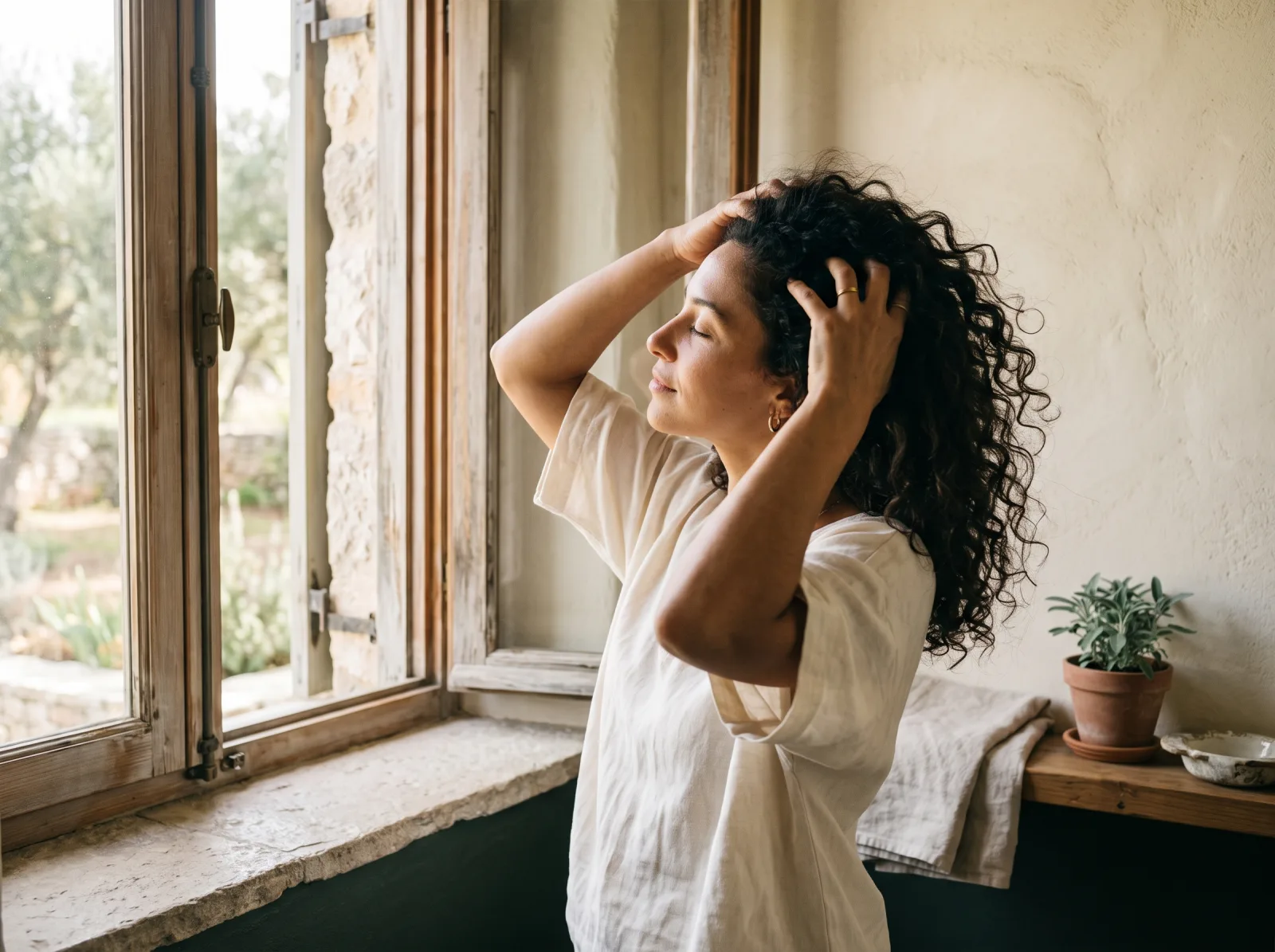 A woman massages her scalp beside a window.